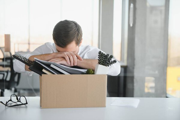 Sad Fired. Let Go Office Worker Packs His Belongings into Cardboard Box and Leaves Office. Workforce Reduction, Downsizing, Reorganization, Restructuring, Outsourcing. Mass Unemployment Market Crisis.