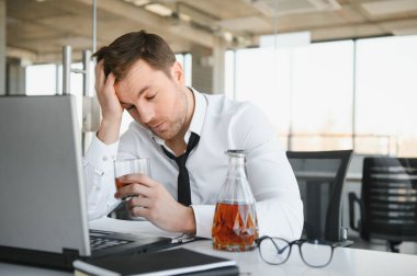 Alcoholism at work. Tired employee drinking alcohol at workplace, can not handle stress
