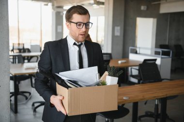 Sad Fired. Let Go Office Worker Packs His Belongings into Cardboard Box and Leaves Office. Workforce Reduction, Downsizing, Reorganization, Restructuring, Outsourcing. Mass Unemployment Market Crisis.