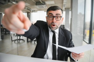 Kızgın işadamı masada oturup bağırıyor.