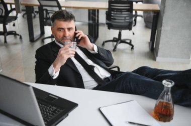 Yaşlı işadamı ofiste içki içiyor..