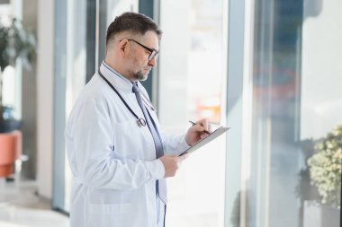 Gözlüklü ve beyaz önlüklü ciddi bir kıdemli doktorun portresi.