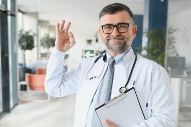 Gözlüklü ve beyaz önlüklü ciddi bir kıdemli doktorun portresi.