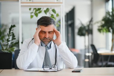 Klinikteki olgun doktor yorgun burnu ve gözleri ovuşturup yorgun ve baş ağrısı çekiyor. Stres ve hüsran kavramı