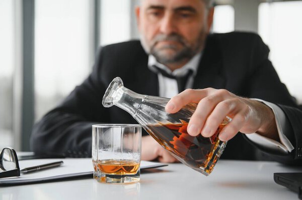 Old male employee drinking alcohol at workplace.