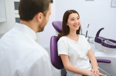 Image of pretty young woman sitting in dental chair at medical center while professional doctor fixing her teeth.