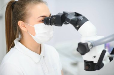 Diş sağlığı muayenehanesinde diş mikroskobu kullanan kadın diş hekimi..