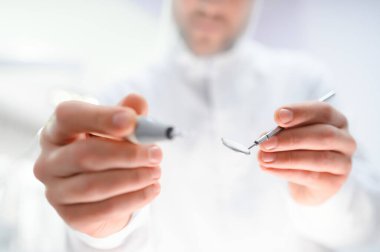 Dipte, kendinden emin, mutlu, profesyonel stomatolog, 20 'li yaşlardaki beyaz cüppeli doktor dişçi bürosundaki dolapta diş delme makinesi olduğunu gösteriyor. Sağlık hizmetleri estetik tedavisi