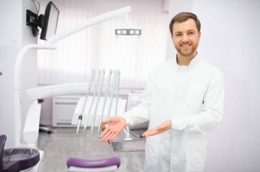 Modern diş muayenehanesinde poz veren doktor önlüklü çekici erkek dişçi..