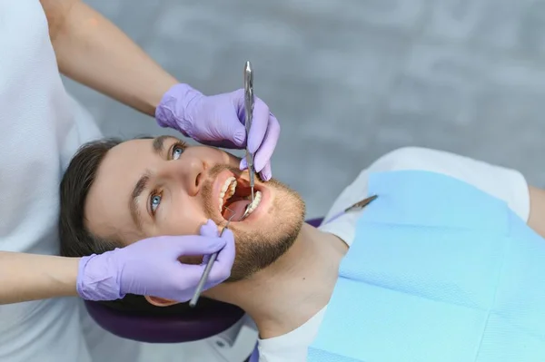 年轻胡子男子坐在牙椅上 参观现代牙科诊所 定期进行检查 女牙医 — 图库照片