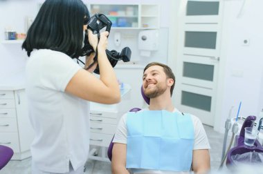 Dişçi kliniği. Bir dişçi, dişçi muayenehanesinde randevusu sırasında müşterisinin dişlerinin fotoğrafını çekiyor.