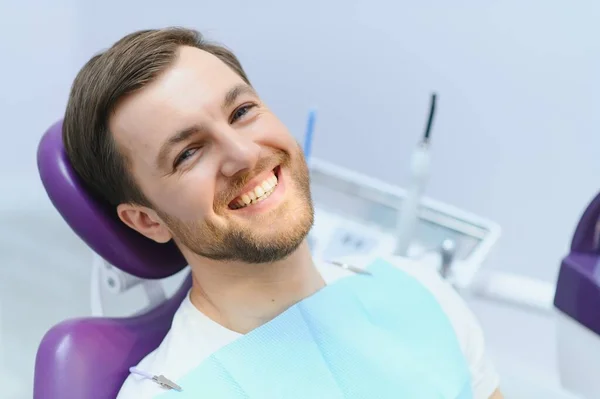 stock image Handsome man smiling while teeth exam. Happy male patient sitting in a dentist's chair and having check up teeth