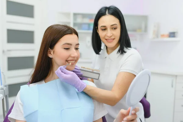Dentist checking and selecting color of young woman's teeth.