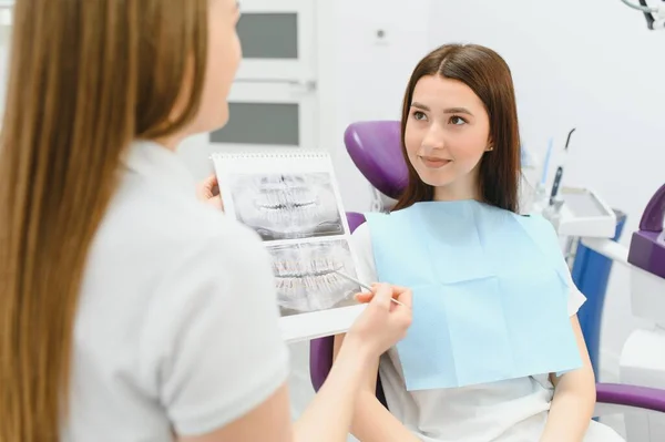 The dentist shows the x-ray image to the patient. People, medicine, dentistry, technology and healthcare concept. Woman dentist with x-ray image of teeth and female patient in dental clinic office