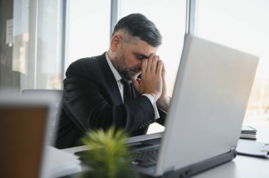 Yorgun bir ofis çalışanı masasında oturup, gözlerini ovuşturduğunu ve yorgun düştüğünü düşünüyor.