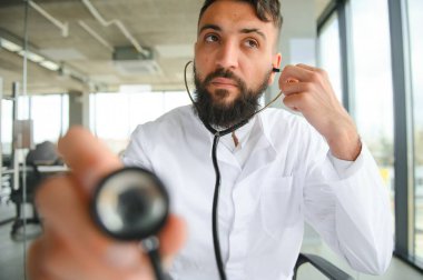 Beyaz önlüklü, yakışıklı, hoş bir Arap erkek doktor, kameraya içeride poz veriyor.