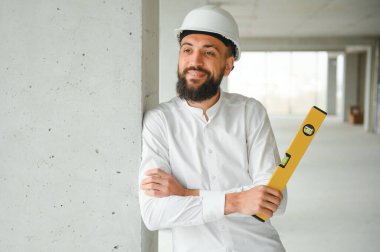 Güvenlik kaskı takan ve inşaat planı tutan yakışıklı Orta Doğulu bir adamın portresi. Çalışanlar ve iş konsepti