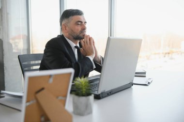 Yorgun bir ofis çalışanı masasında oturup, gözlerini ovuşturduğunu ve yorgun düştüğünü düşünüyor.