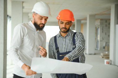İnşaat alanındaki projeyi tartışan çok ırklı erkek çalışanlar..