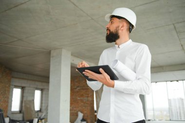 Güvenlik kaskı takan ve inşaat planı tutan yakışıklı Orta Doğulu bir adamın portresi. Çalışanlar ve iş konsepti