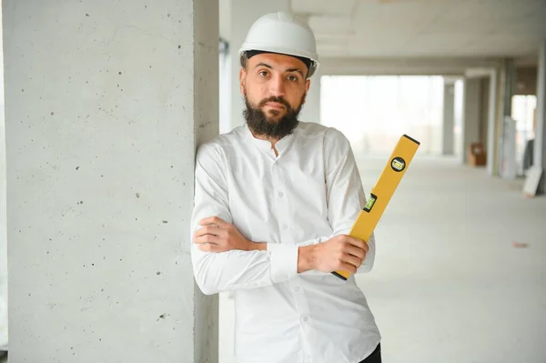 Serious busy young attractive arabic industrial engineer in hard hat with project drawings in factory interior. Professional and industry, builder architect job, worker checking work at plant indoor.