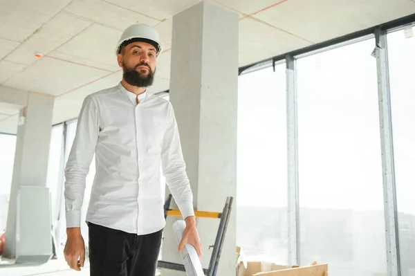 Serious busy young attractive arabic industrial engineer in hard hat with project drawings in factory interior. Professional and industry, builder architect job, worker checking work at plant indoor.