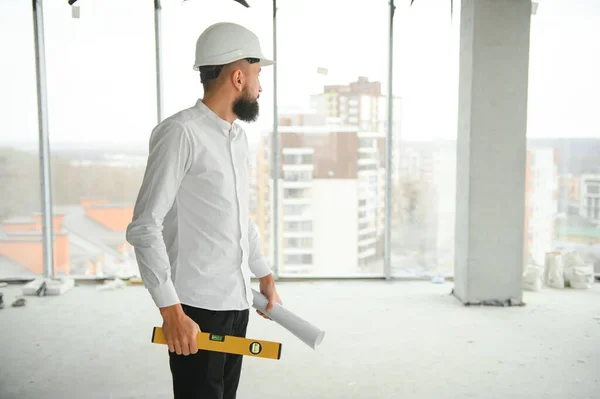 Serious busy young attractive arabic industrial engineer in hard hat with project drawings in factory interior. Professional and industry, builder architect job, worker checking work at plant indoor.