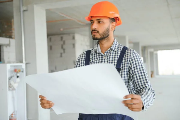 stock image Indian construction site manager standing wearing helmet, thinking at construction site. Portrait of mixed race manual worker or architect