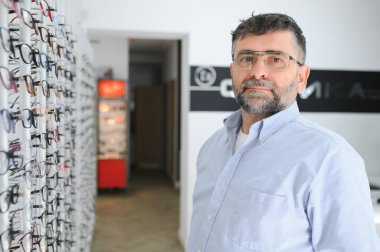 Erkek müşteri optik mağazasında gözlük seçiyor.