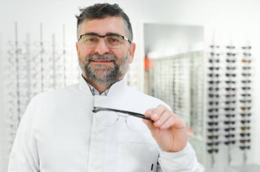 Deneme için gözlük tutan yakışıklı bir göz doktoru. Optometrist gözlük takmayı teklif ediyor. Ellere ve gözlüklere odaklanmış küçük alan defi ile görüntü.