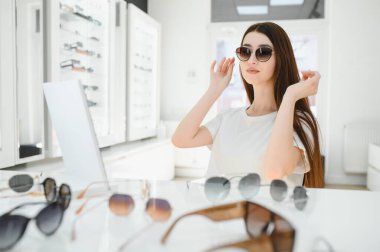 O seçimini yaptı. Güzel genç bir kadın yeni güneş gözlüğünü takıyor ve optik mağazasında dururken gülümsüyor.
