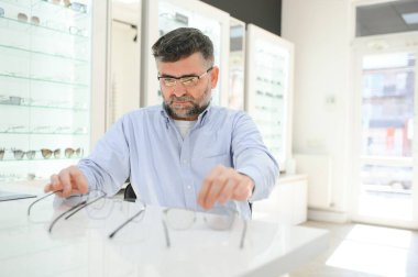 Erkek müşteri optik mağazasında gözlük seçiyor.