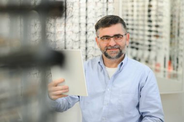 Yakışıklı son sınıf öğrencisi gözlük çerçevesini optik mağazada seçiyor.