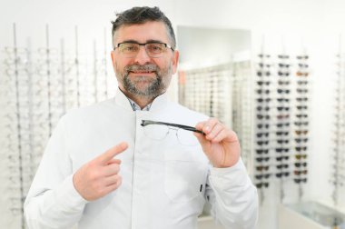 Deneme için gözlük tutan yakışıklı bir göz doktoru. Optometrist gözlük takmayı teklif ediyor. Ellere ve gözlüklere odaklanmış küçük alan defi ile görüntü.