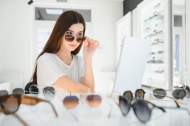 Mağazada duran ve aynanın yanında güneş gözlüğü takan genç bir kadının portresi.