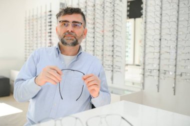 Yakışıklı son sınıf öğrencisi gözlük çerçevesini optik mağazada seçiyor.