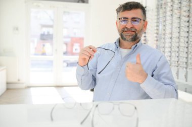 Son sınıf öğrencisi optik mağazada gözlük seçiyor. Mükemmel olana karar vermek için gözlük çerçevesi dene..