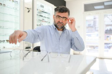Son sınıf öğrencisi optik mağazada gözlük seçiyor. Mükemmel olana karar vermek için gözlük çerçevesi dene..