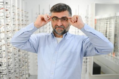 Erkek müşteri optik mağazasında gözlük seçiyor.