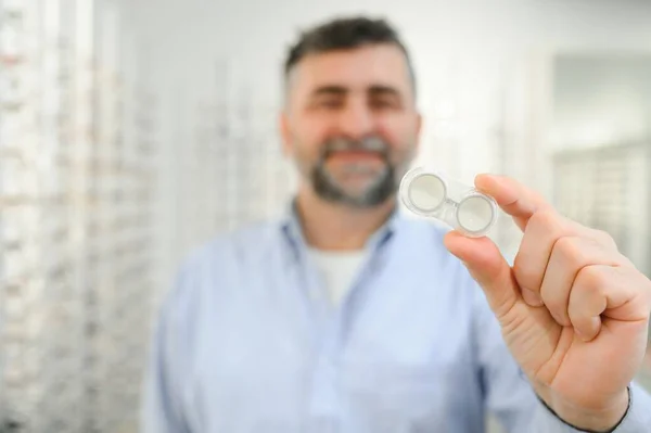 man holding contact eye lenses and container in hand, applying eye contacts from lens box.