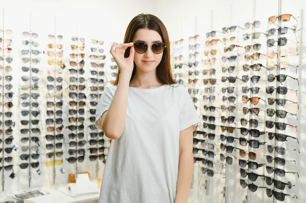她做出了选择 漂亮的年轻女子站在眼镜店里调整着她的新太阳镜 微笑着 — 图库照片