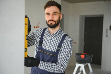 Mavi sakallı yakışıklı tamircinin portresi. Gömleği kollarını kavuşturmuş, kameraya bakıyor..