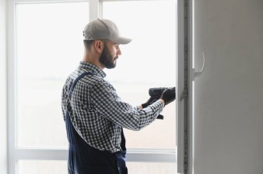 Evdeki oturma odasına plastik pencereler monte eden ya da ayarlayan işçi.