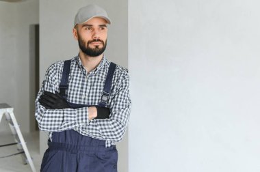 Mavi sakallı yakışıklı tamircinin portresi. Gömleği kollarını kavuşturmuş, kameraya bakıyor..