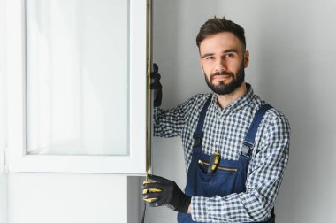 Mavi sakallı yakışıklı tamircinin portresi. Gömleği kollarını kavuşturmuş, kameraya bakıyor..