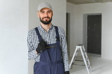 Gülümseyen tamirci merdivenin yanında durup kameraya bakıyor..