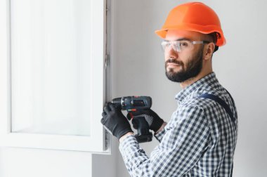 Evdeki oturma odasına plastik pencereler monte eden ya da ayarlayan işçi.