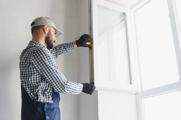 Worker installing plastic window indoors.