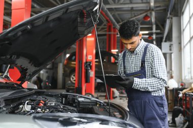 Latin otomobil tamircisi otomobil servisinde çalışırken bir arabayı inceliyor..