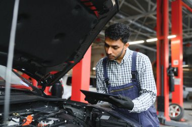 Adam araba teknisyeni motor tamir sorunu, sistem kontrolü sırasında, araba garajında bakım ve onarım için tablet bilgisayar kullanarak